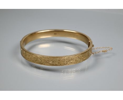 A 9ct yellow gold oval half-hinged bangle with foliate decoration, concealed clasp and safety chain attached, approx 10g 