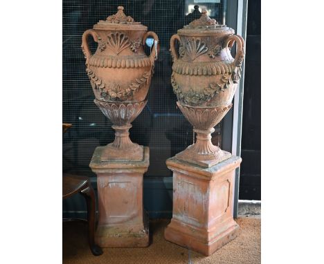 A large pair of weathered classical cast terracotta lidded urns, with twin loop handles and decorated with floral leaf swags,