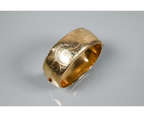 A 9ct yellow gold oval half-hinged wide bangle with chased foliate decoration (missing safety chain), 2.5 cm wide, 6.5 cm dia