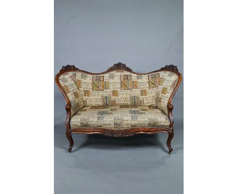 A late Victorian oak double spoon back sofa, with Latin alphabet tapestry style fabric, raised on cabriole front legs to bras