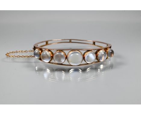 A Victorian oval half-hinged bangle of open wirework form, set with seven graduated circular cabochon moonstones, yellow meta