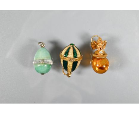Three various egg-shaped pendants - one pale green hardstone, one green and pale yellow enamel, and one amber with gilt metal