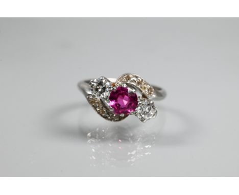 A ruby and diamond ring, the central ruby with a diamond to each side in crossover setting, with diamond set scrolls above an