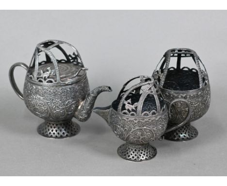 An antique Indian low grade white metal tea service, finely chased with flowers and foliage beneath cobra-basket rims, scroll