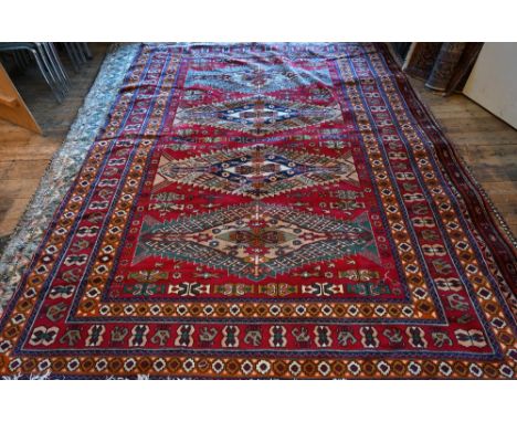 A Caucasian design red ground carpet with four geometric  medallions, repeating red/orange borders, 310 x 229 cm