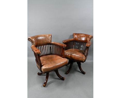 Amended - A matched pair of vintage brass studded brown leather and stick-back captains chairs, raised on swivel bases, good 