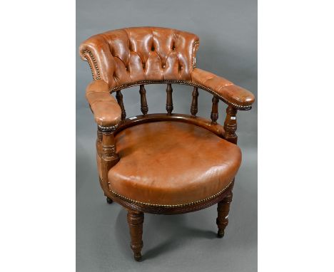 An Edwardian walnut framed buttoned tan leather armchair, raised on turned front legs and roller castors