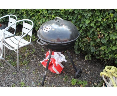 A circular metal barbeque with vented lid, on tripod trolley base, with a small quantity of charcoal