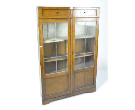 An oak glazed bookcase, a pair of short drawers positioned above the twin panelled doors, opening to reveal shelves, on brack
