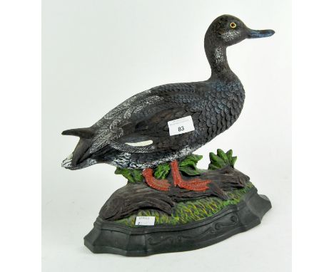 A painted cast iron duck door stop, the duck standing on a tree trunk on a grassy bank, height 29.5cm