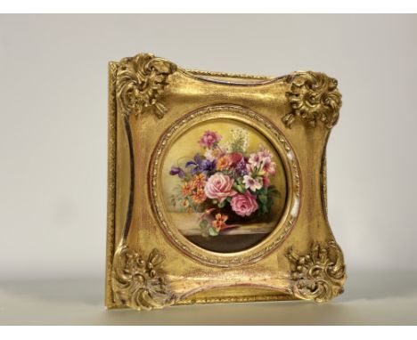 A Royal Worcester porcelain plaque painted by Ernest Phillips, circular, depicting a floral still life on a ledge, signed to 