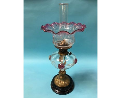 An Edwardian oil lamp, with flared cranberry shade and clear glass reservoir