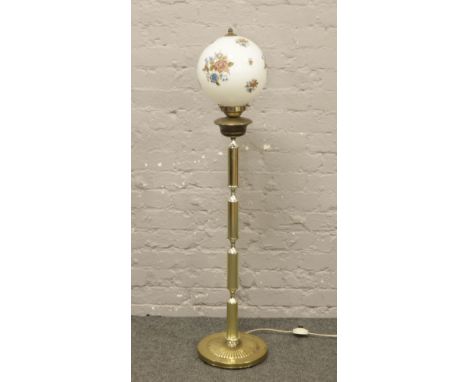 A gilt metal standard lamp with opaque glass globe shade decorated with roses.