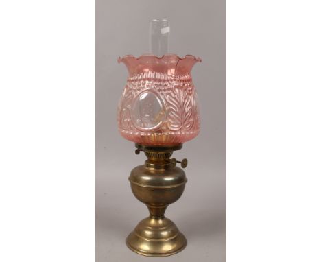 A brass based oil lamp with cranberry coloured pressed glass shade.
