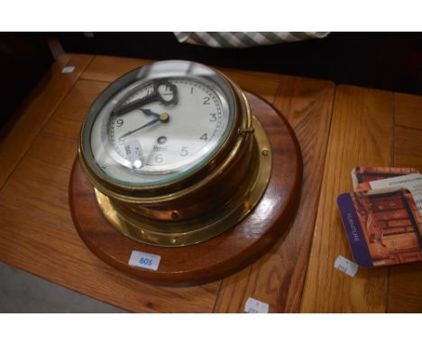 A porthole style brass clock mounted on mahogany plinth