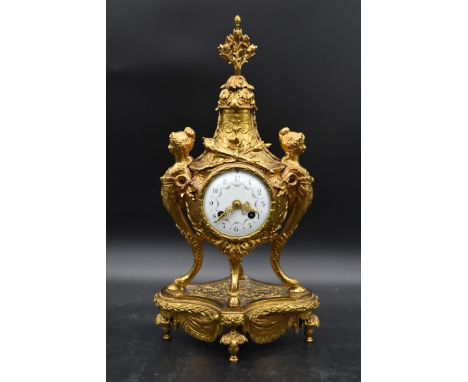 A French style brass mantel clock with garland and pineapple finial, the enamel face supported by female satyr figures on a p