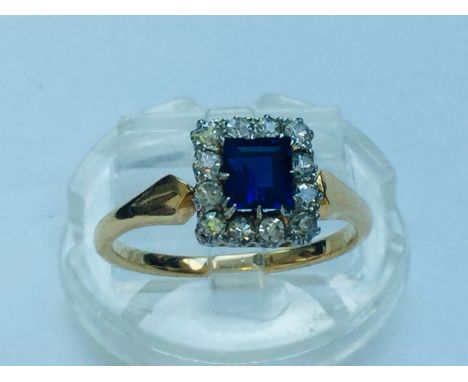 An 18ct gold sapphire and diamond ring, centrally set with a princess cut sapphire measuring 4 x 5mm, surrounded by 12 x roun