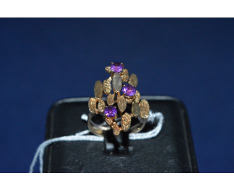 Amethyst dress ring, set with three amethysts amongst plain and textured plaques, on 9ct yellow gold shank, ring size N.