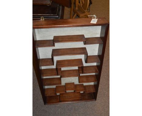 A stained Oriental hardwood wall-mounted display shelf unit with stepped shelves against a cloth covered back panel, 56cms wi