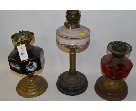 Three duplex oil lamps, to include: a brass lamp with red glass reservoir a brass column style lamp with pink and fruit theme