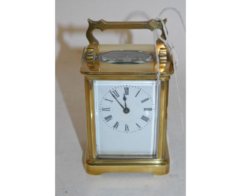 A brass carriage clock with white face and Roman dial, key present.