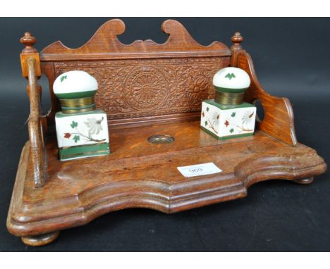 A vintage 20th Century oak ink stand. Having a decorated carved back, with two ceramic hand painted ink pots with hinged roun