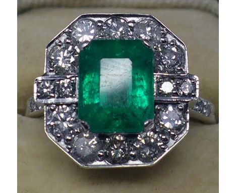 An 18ct white gold emerald and diamond cluster ring centrally set with a stepped-cut rectangular emerald to outer emeralds an