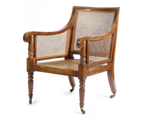 A George IV mahogany bergère armchair in the manner of Gillows, with a cane back, sides and seat, with ribbed arm supports an