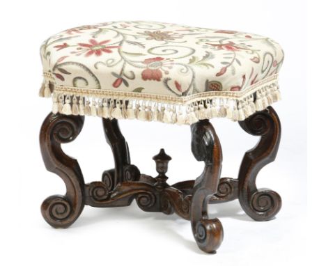 An oak stool, with a needlework seat with a tasselled fringe, on scroll carved legs united by an 'X' stretcher with an urn fi