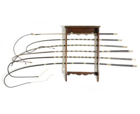 A mahogany wall hanging whip rack, for seven whips, together with six leather and brass whalebone driving whips, three by Cra