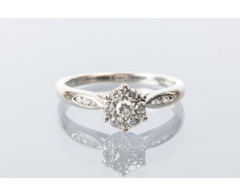 DIAMOND CLUSTER RING
the floral motif bezel set with round stones, on channel set diamond shoulders, in eighteen carat white 