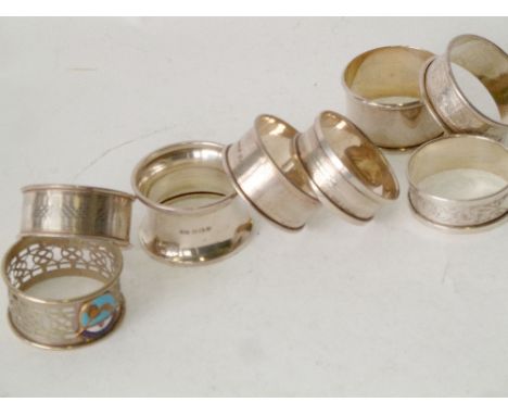 SEVEN VARIOUS HALLMARKED SILVER NAPKIN RINGS, 2.15oz (gross) AND A PIERCED PLATED NAPKIN RING, enamelled Wembley 1824 crest (