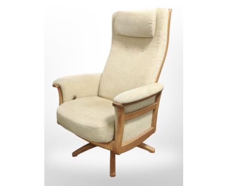 An Ercol elm reclining swivel armchair in beige upholstery.