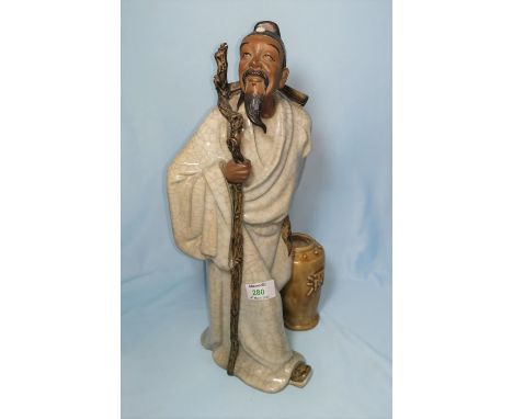 A large Chinese stoneware figure of a man with staff and water jar, having crackle glaze robes and bisque head and hands, hei