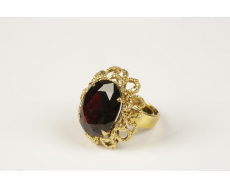 A LARGE GARNET COCKTAIL RING, the oval-cut garnet in a textured open loop 18ct yellow gold surround, the shank stamped '18K'.