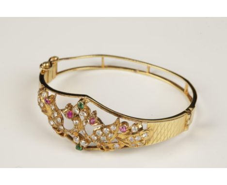 AN INDIAN GEMSTONE BANGLE, the unmarked yellow metal bangle, hinged, the top half modelled as a pair of love birds and set wi