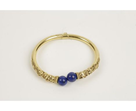 A CONTINENTAL UNMARKED YELLOW GOLD TORQUE BANGLE, hinged, with applied vine and grape decoration, terminating in lapis lazuli