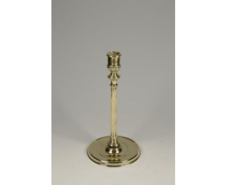 A FRENCH BRASS CANDLESTICK with a dished circular base supporting a fluted stem and a gadrooned nozzle with a knop below, cir