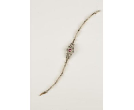 A BELLE EPOQUE RUBY AND DIAMOND BRACELET, the pink-tone ruby in an open diamond-set scroll surround, on an elasticated strap,