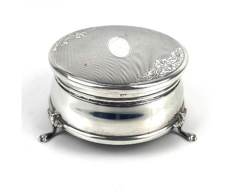 A modern silver trinket box. The hinged lid with engine turned and foliate engraved decoration, raised on triple feet, blue v