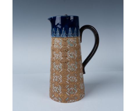 A pitcher with a blue rim featuring high relief art of pine trees and a gilded body depicting intricate snowflake like patter
