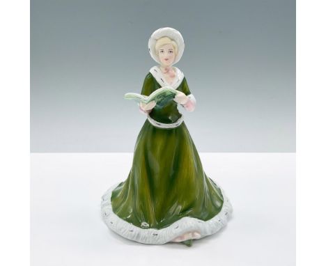 A blonde woman sings carols from a songbook, wearing a festive forest green dress with white fur trim around the base, cuffs,
