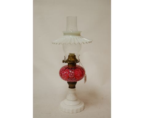 A circa 1900 oil lamp, having a milk glass filled shade above a cranberry glass reservoir, on milk glass pedestal base