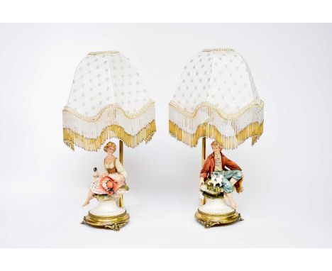 A pair of Capodimonte porcelain table lamps by Cazzola, modelled as a rustic boy and girl seated on rocky outcrops, mounted o