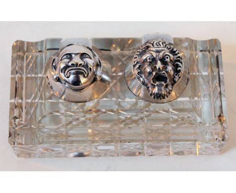 A cut glass inkwell or standish having hallmarked silver grotesque masked hinged lids, length 11.5cm.Condition: Very minor ch