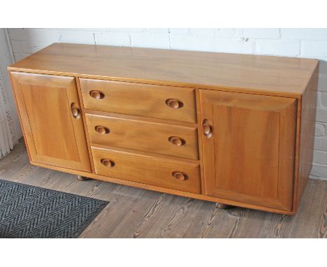 An Ercol light elm sideboard having three central drawers flanked by two cupboards and raised on castors, length 155.5cm, dep