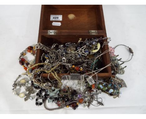 A wooden jewellery box containing a quantity of predominantly white metal costume jewellery - This lot MUST be paid for and c