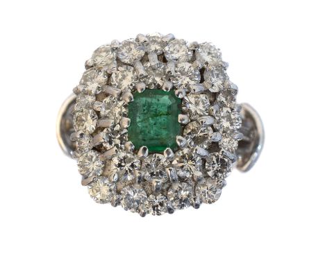 An emerald and diamond cluster ring. The rectangular shape emerald within a brilliant cut diamond tiered surround, estimated 