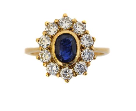 A sapphire and diamond cluster ring. The oval shape sapphire within a brilliant cut diamond surround, estimated total diamond
