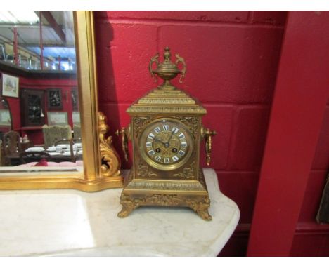 An early 20th Century ornate brass mantel clock with urn finial and twin handles, painted enamel Roman numeral dial, striking